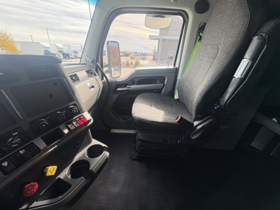 Kenworth T680 truck interior from passenger side showing driver seat, dashboard, controls, and steering wheel; visible window and exterior parking lot.