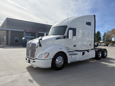 Kenworth T680 sleeper cab tractor in white, side view, with chrome wheels and dual rear axles; dealership building in background.