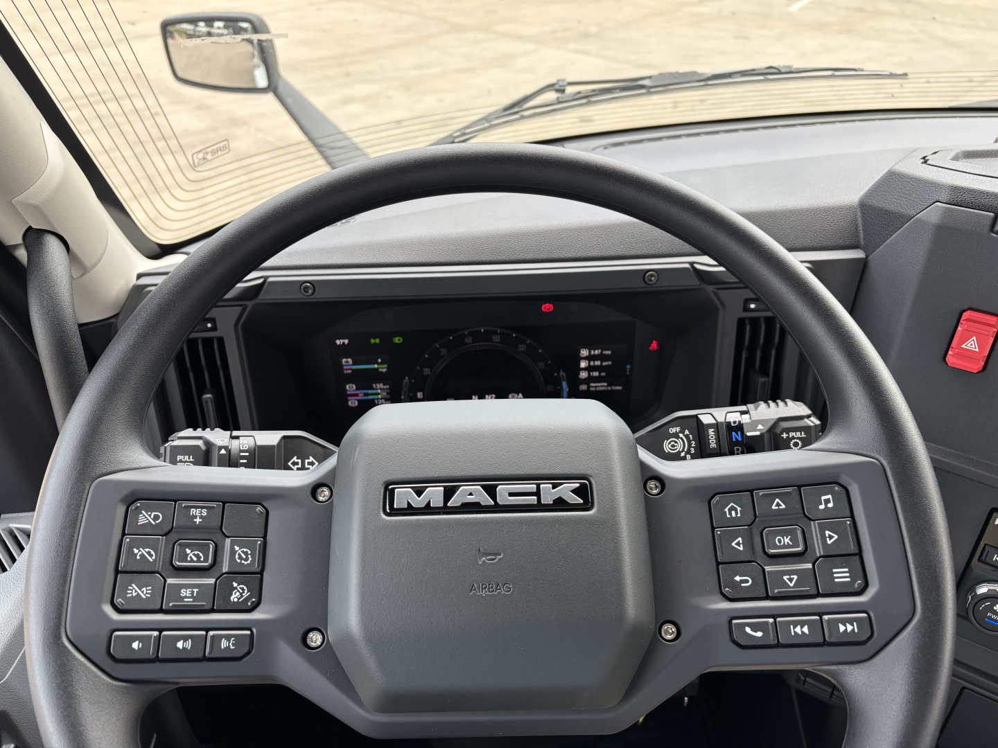 Interior view of a new 2027 Mack AN64 dump truck showing steering wheel with MACK logo and instrument cluster.