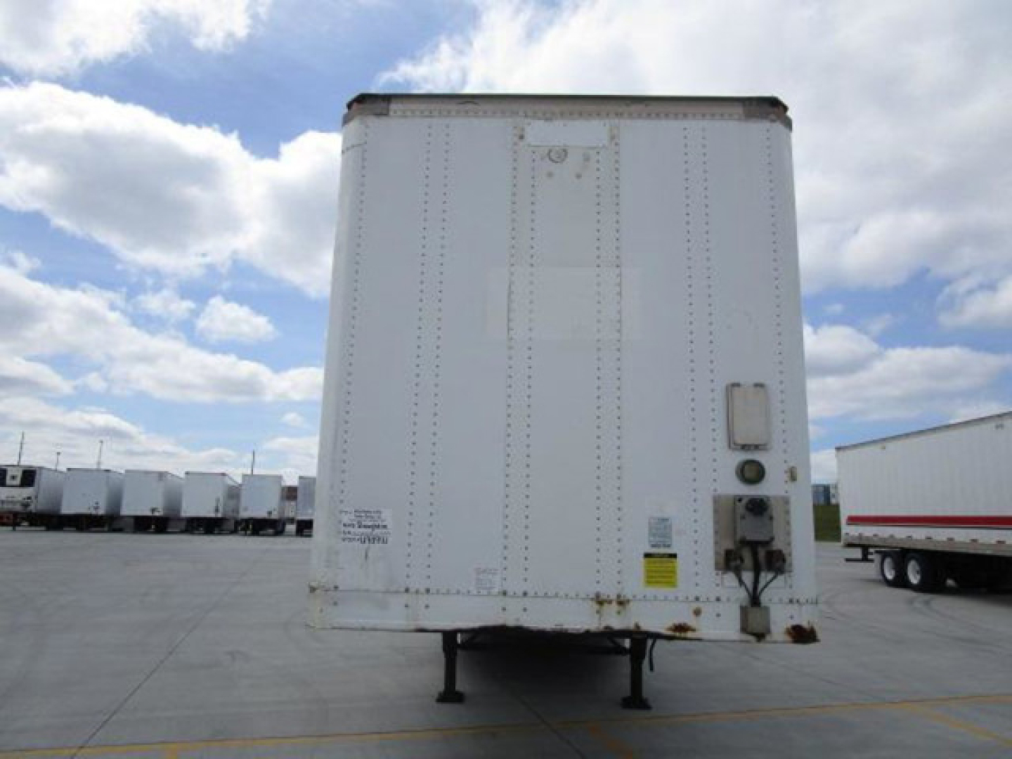 Rear view of a white 2014 Stoughton van trailer with a stand at the back, showing riveted metal exterior, door area, and a couple of warning labels.