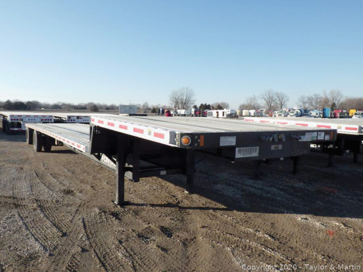 Flatbed trailer showing Fontaine Infinity model in a used stock lot with long deck and ramp legs visible.