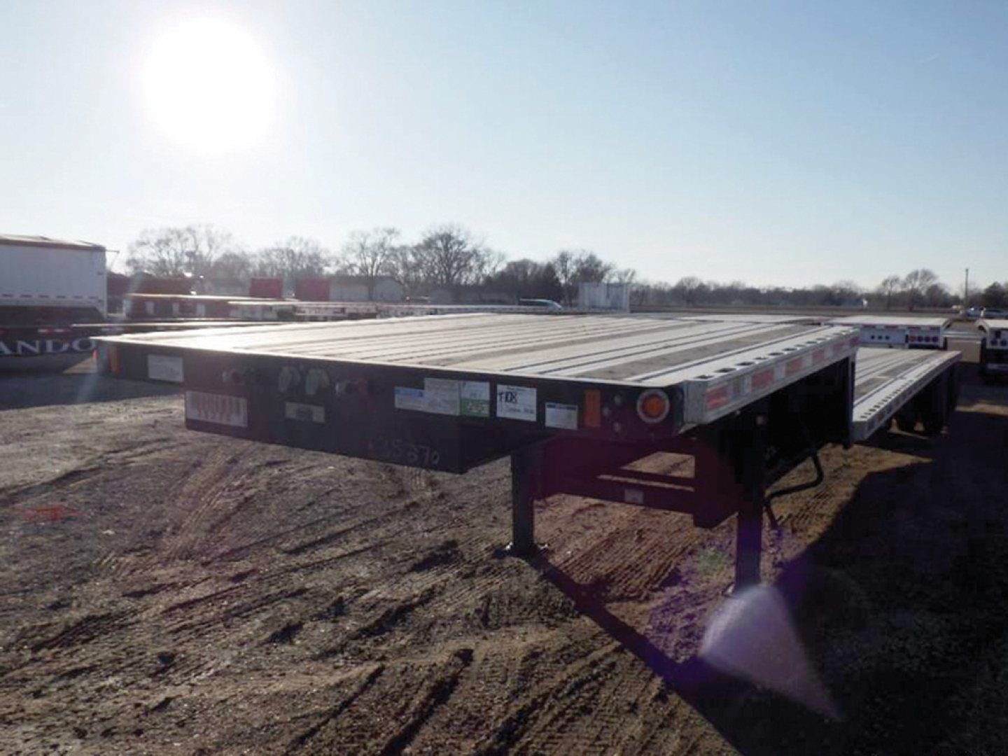 Flatbed trailer in an outdoor lot showing a Fontaine Infinity drop deck with decals and a gooseneck support, warning labels along the edge and reflective lights.
