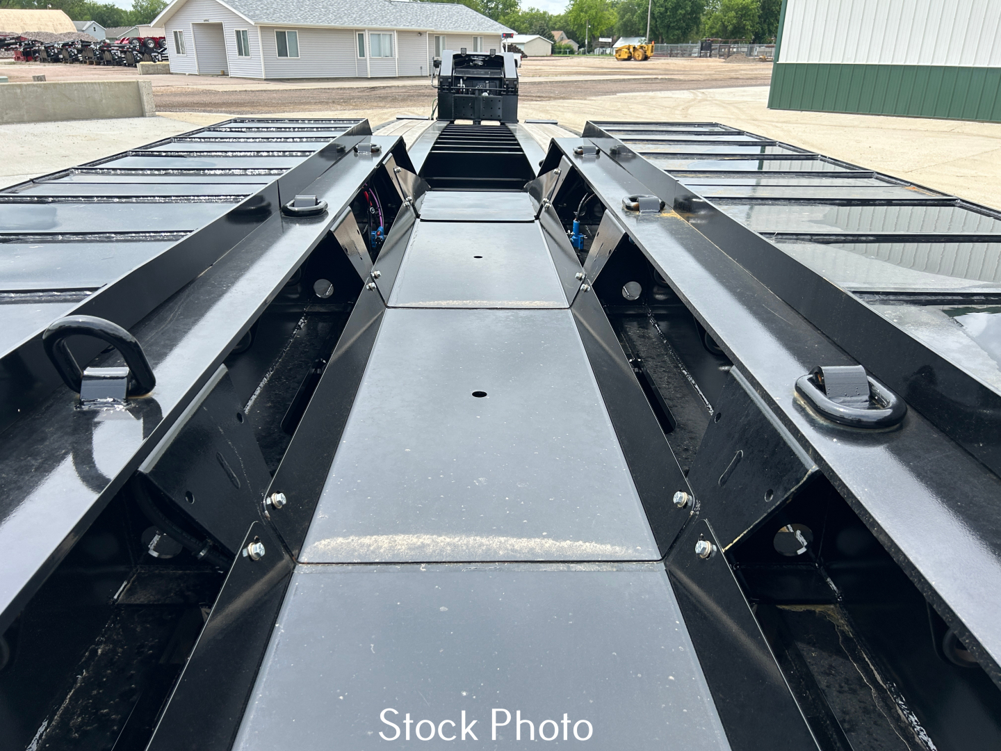 Truck trailer deck view showing long black metal frame rails, winches, and mid-section with sturdy side rails and gooseneck area; no general markings visible.