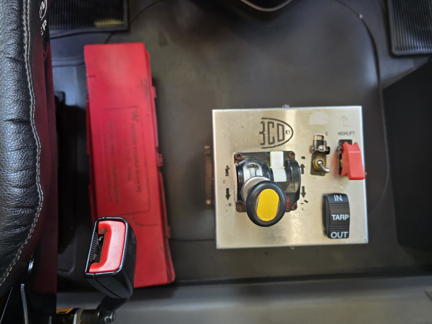 Dashboard panel with 3ED logo, round yellow knob, black toggle switch, red emergency lever; visible text includes IN, TARP, OUT on a metallic control plate inside a Mack Granite truck.
