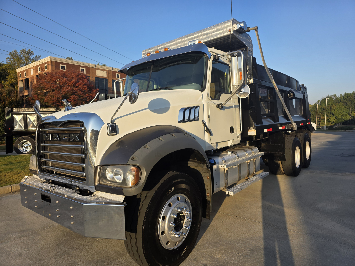 Mack Granite dump truck with white cab and black dump bed, front grille with Mack branding, large bumper, dual rear axles, side steps, and chrome fuel tanks.