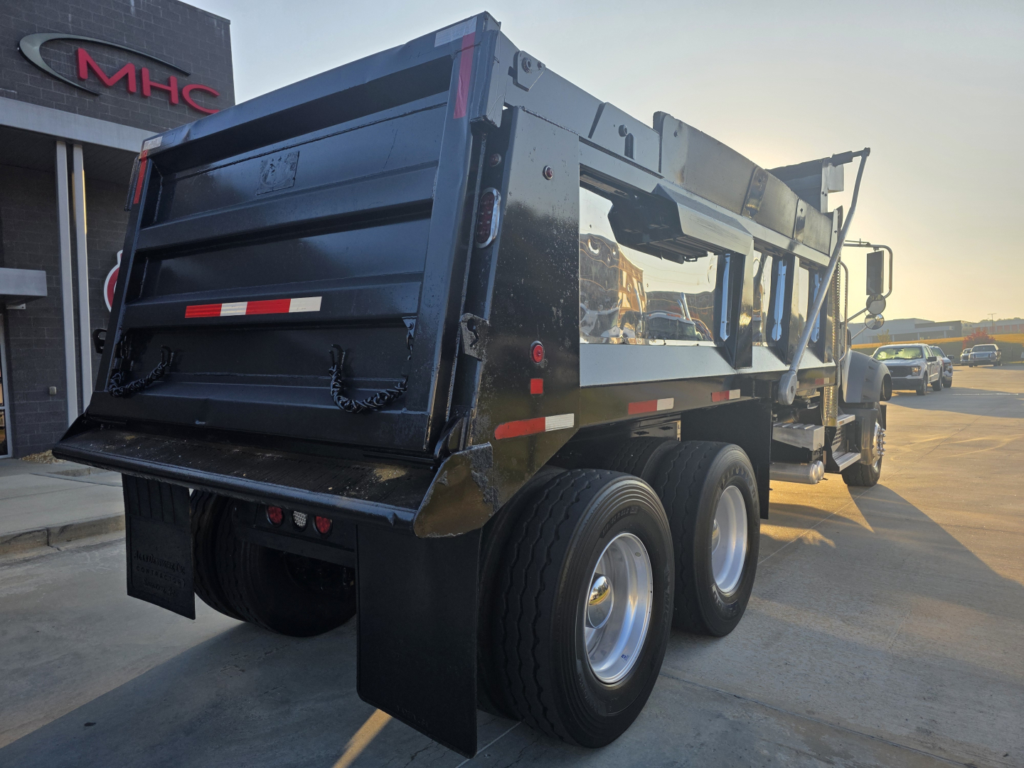 Dump truck rear/side view showing a Mack Granite dump bed with dual rear axles and heavy-duty chassis, black exterior, reflective strips, and taillights.