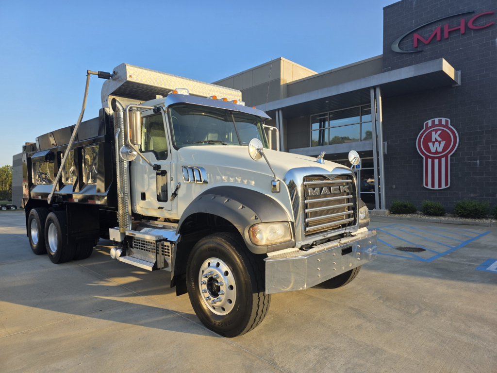 Mack GRANITE dump truck in front of dealership, chrome grille with Mack emblem, dual rear axles, dump bed, daylight, VIN 1M2GR2GC6NM025884