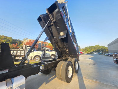 Dump truck bed tilted showing hydraulic cylinder and dual rear wheels with thick tires.