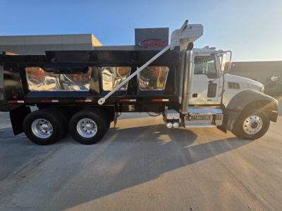 Dump truck showing Mack GRANITE in-service with black dump bed and white cab, side view, drivetrain and dual rear axles visible.