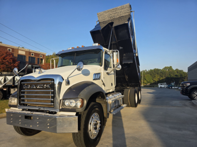 Dump truck (2022 Mack Granite) white cab with black dump bed raised, front grille and bumper, side mirrors, and wheel in view.