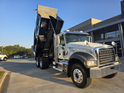 Dump truck in service position showing Mack Granite front grille, dual rear axles, and a raised dump bed with hydraulic mechanism.