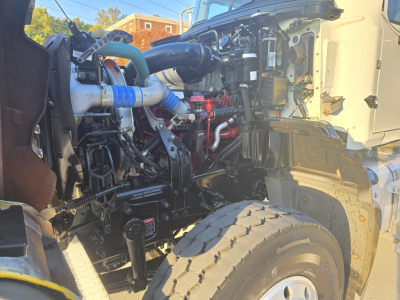 Truck engine bay close-up showing blue coolant hoses, black intake tubing, red intercooler piping, and exposed engine components in a Mack Granite dump truck.