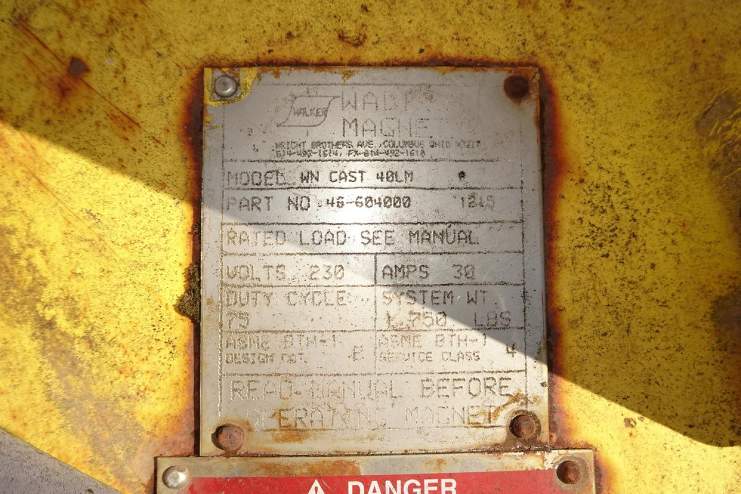 Metal data plate on yellow machinery showing model HN CAST 40LM, part number 46-604000, rated load, volts 230 amps 30, duty cycle, serial numbers, and manufacturer markings.