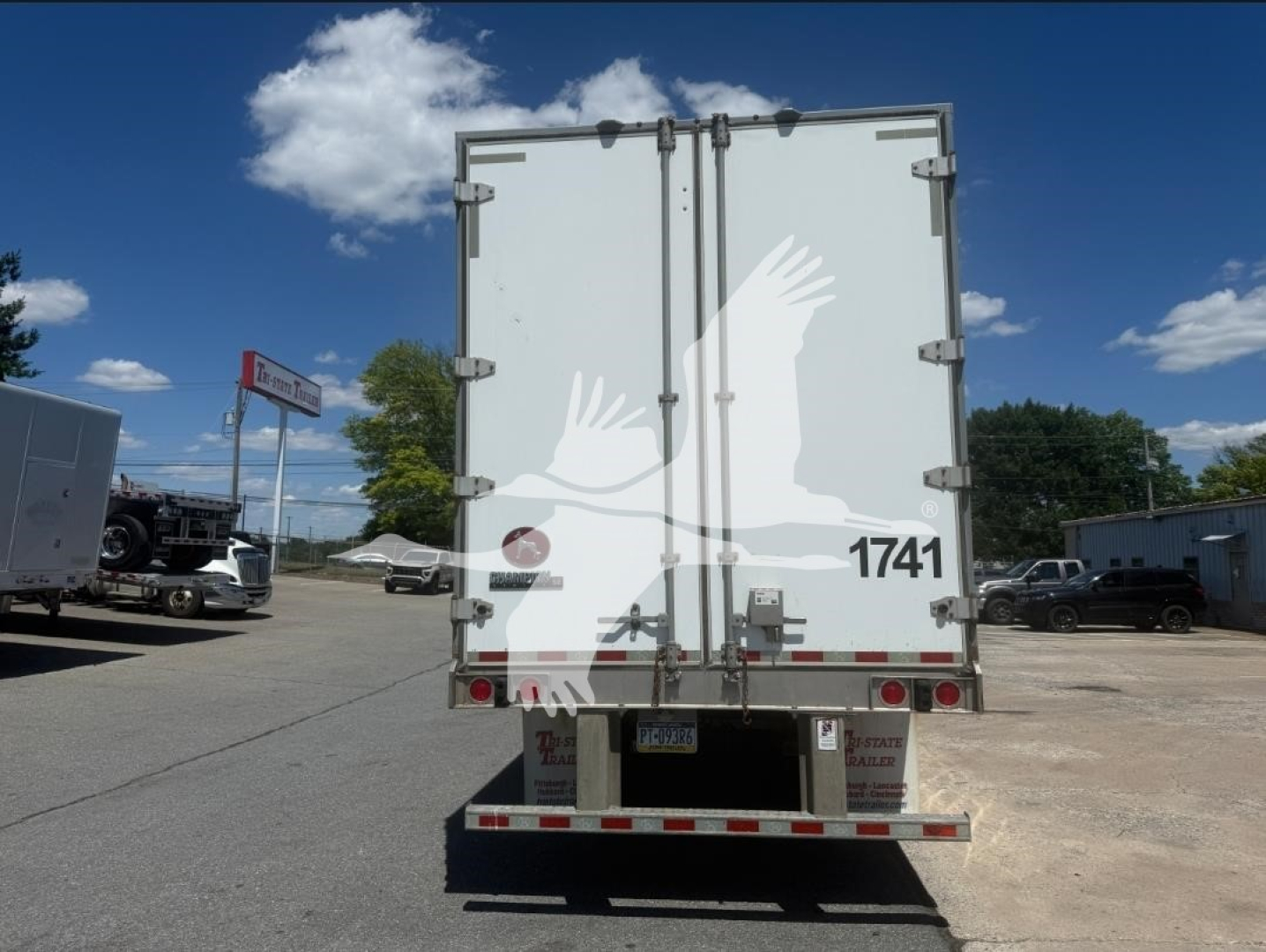 Rear of a white box trailer with double doors, taillights, and bumper. The doors have metal hinges, latches, and a small red circular light. License plate area and reflective tape along bottom. The number 1741 printed on the lower right of