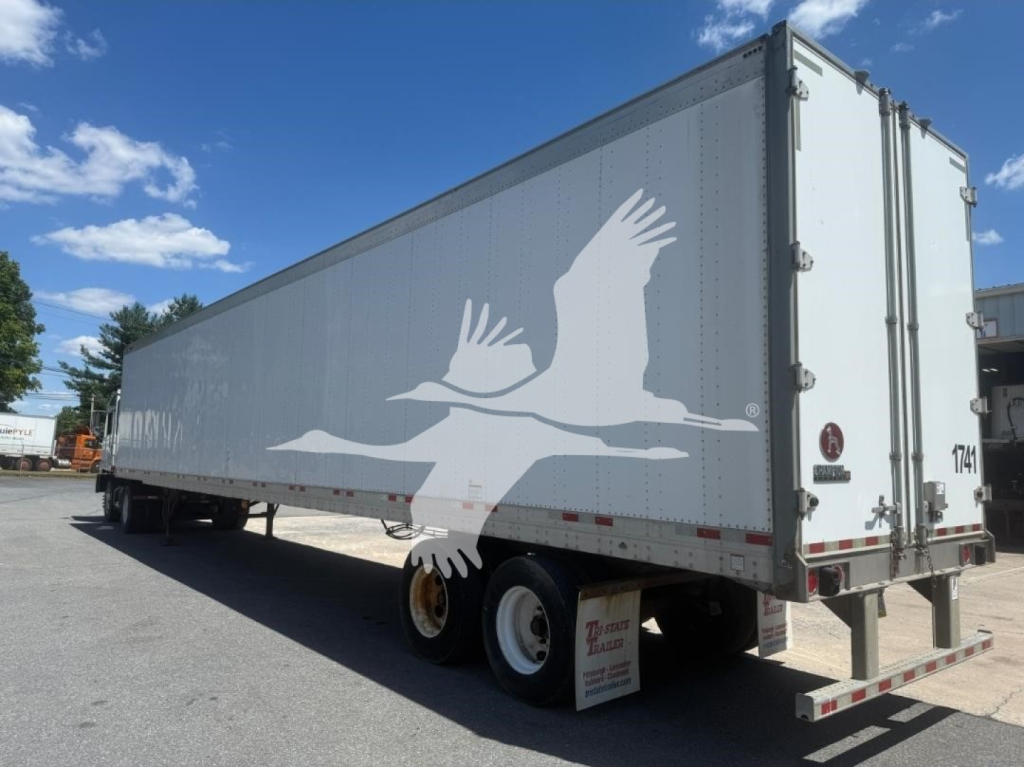 Great Dane trailer in a yard, side and rear view showing white graphic of a flying bird on a gray trailer with double rear doors.