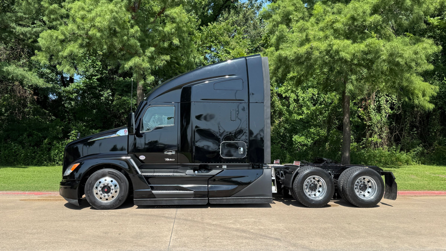 Kenworth T680 tractor cab side view showing aerodynamic profile and dual rear axles with black paint and chrome wheels.