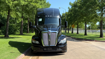 Kenworth T680 front view showing cab, grille, and headlights in a park setting.