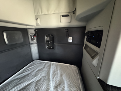 Kenworth T680 cab interior showing sleeper area with light gray upholstery, window panel, and control cluster.