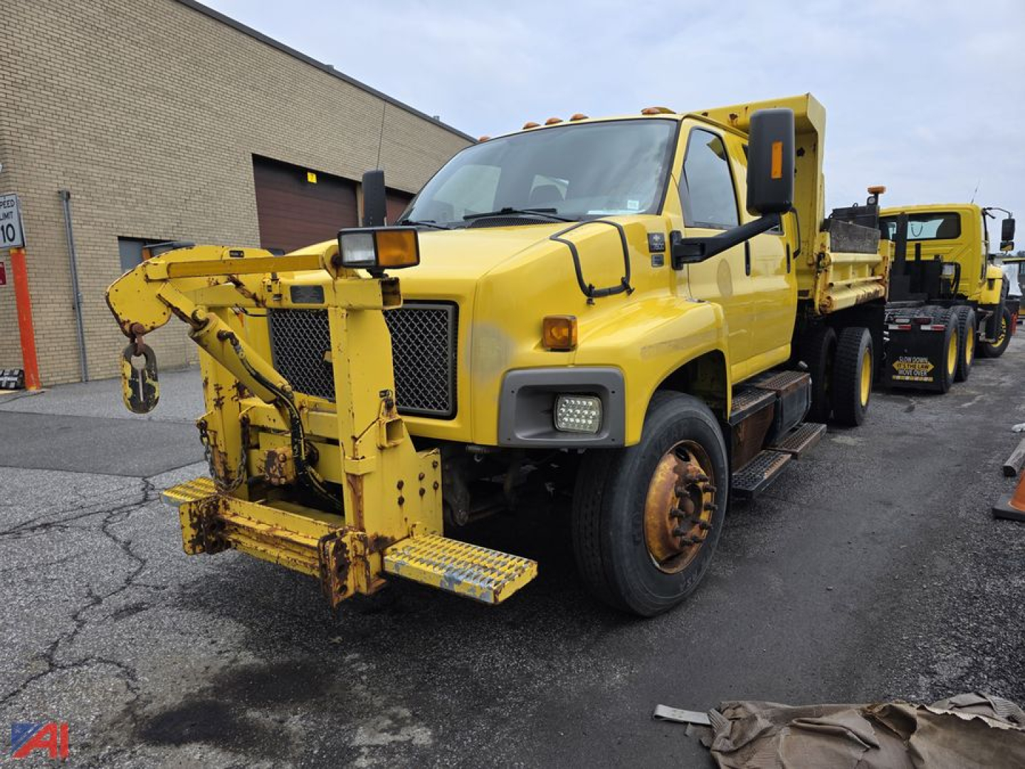 Chevrolet Kodiak C7500 dump truck with front-mounted snow plow attachment. Yellow color, cab with large side mirrors, headlights, and wheel wells.