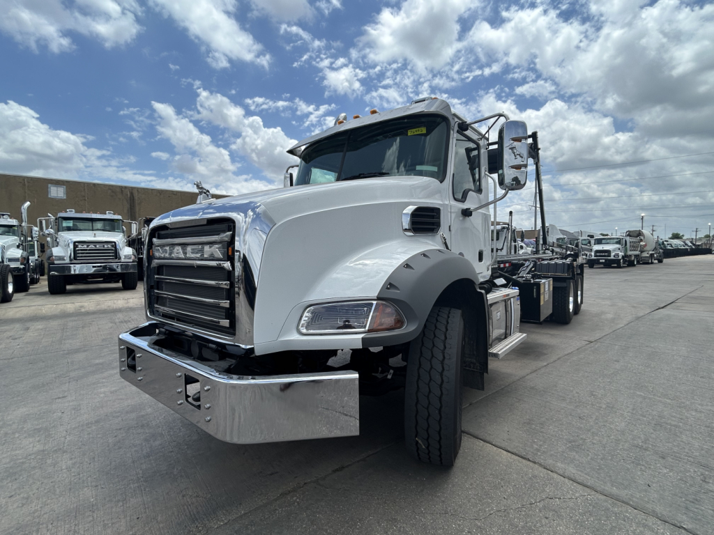 Roll-off truck cab showing Mack GR64B with chrome bumper and grille, white exterior, large front fenders, and side mirrors.