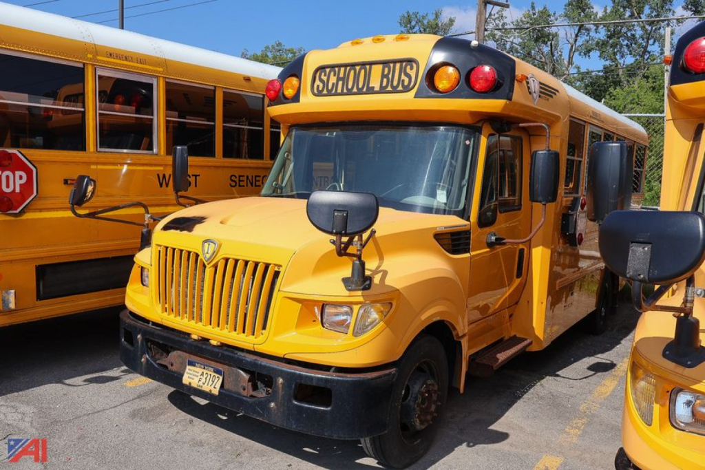 IC Corporation AE series school bus front-right view showing yellow body, stop sign, and 'SCHOOL BUS' sign on roof; adjacent bus in background.