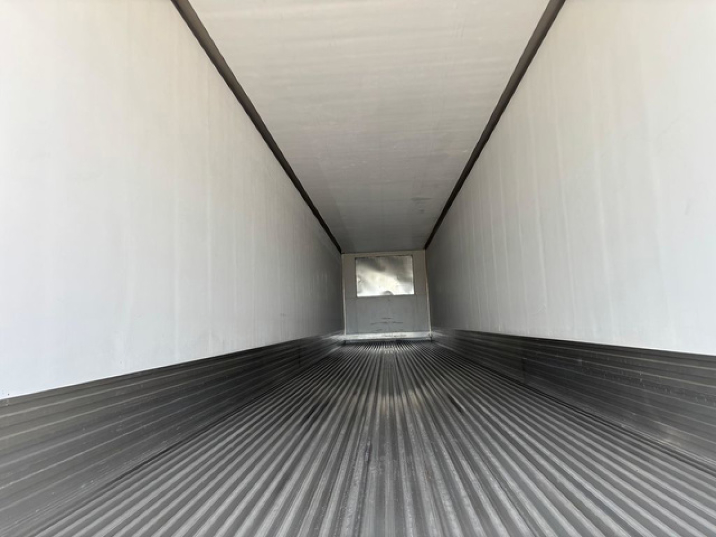 Interior of a new refrigerated utility trailer with ribbed floor and white sidewalls; rear door opening visible in distance.