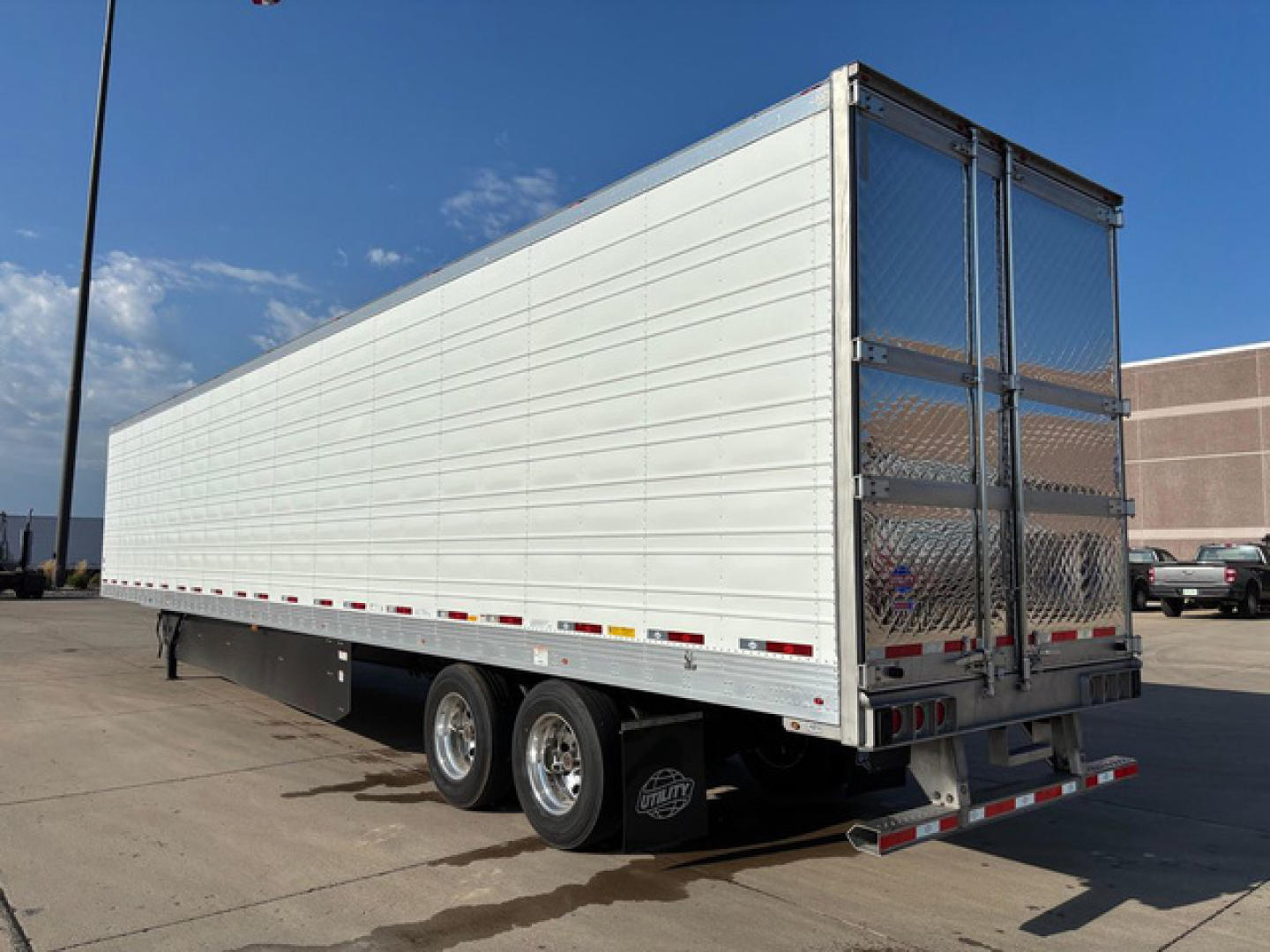 Utility refrigerated trailer side and rear showing aluminum panels and tandems with rear doors and metal chain-link interior visible.