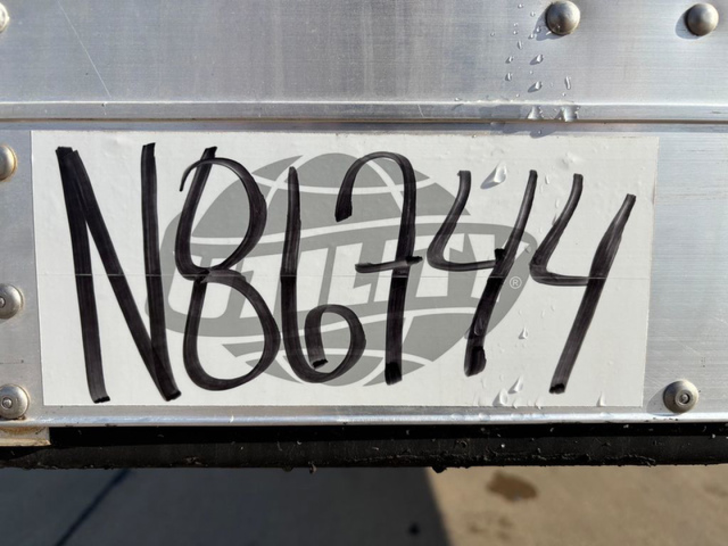 Trailer rear showing bold handwritten VIN N86744 on metal plate with rivets and aluminum surface.