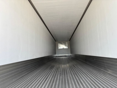 Interior of a new refrigerated utility trailer with ribbed floor and white sidewalls; rear door opening visible in distance.
