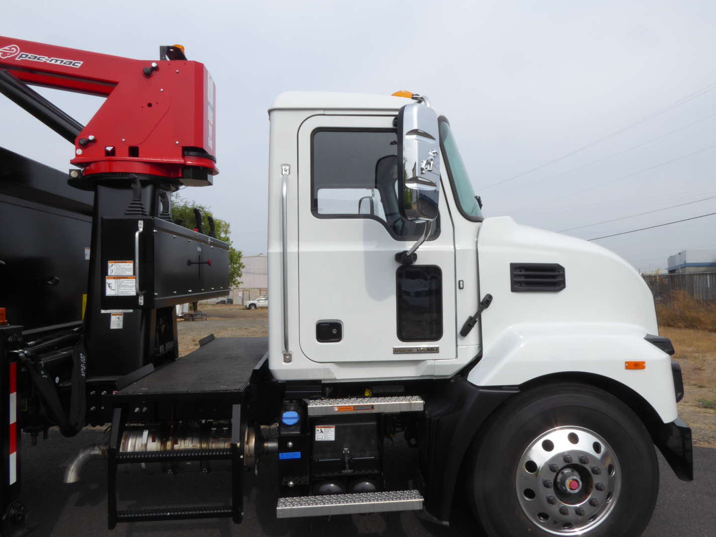 Truck side view showing white cab of a 2025 Mack MD7 grapple truck with red crane attachment and alloy wheels.