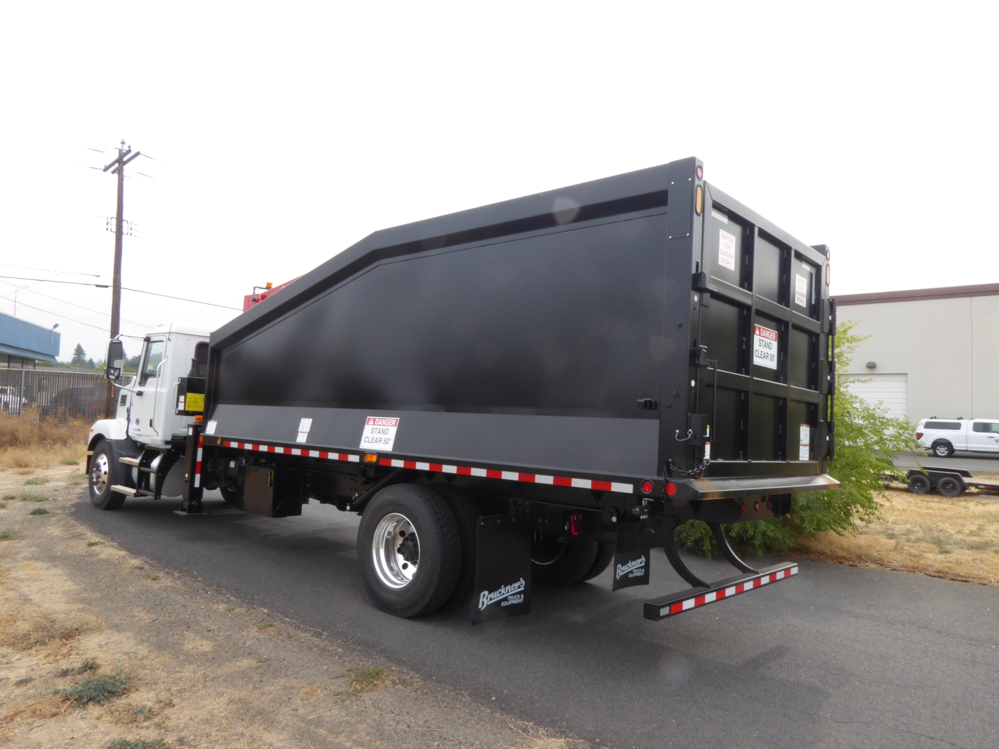 Truck bed and cab of a 2025 Mack MD7 grapple truck with large black dump body, side and rear safety rails, rear underride guard, and dual rear wheels.
