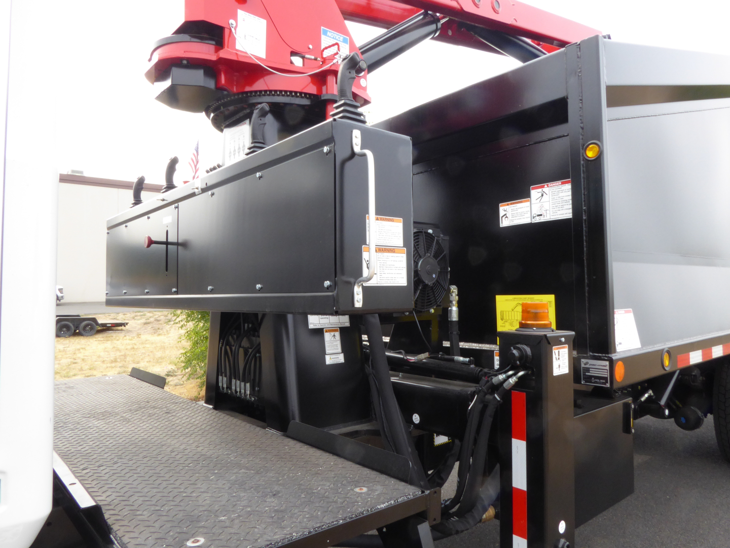 Truck bed with hydraulic grapple and control cabinet for a 2025 Mack MD7, side view showing equipment and hydraulic lines.