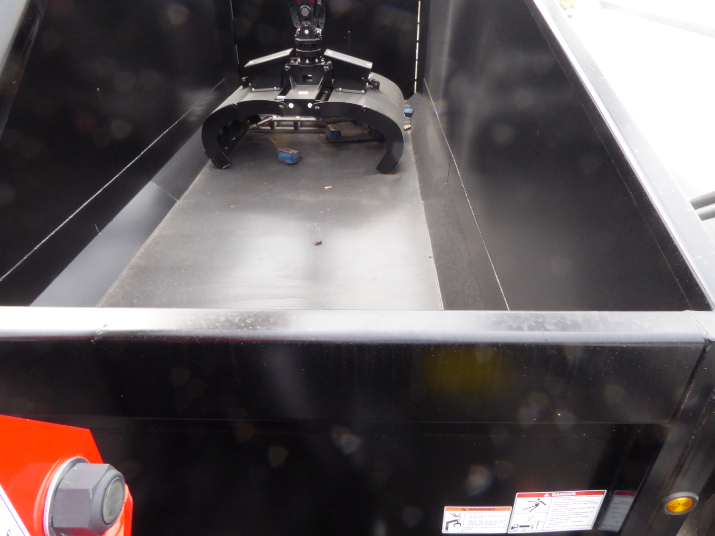 Truck bed interior with a grapple attachment mounting frame visible in the back, along with a small label and interior metal surfaces.
