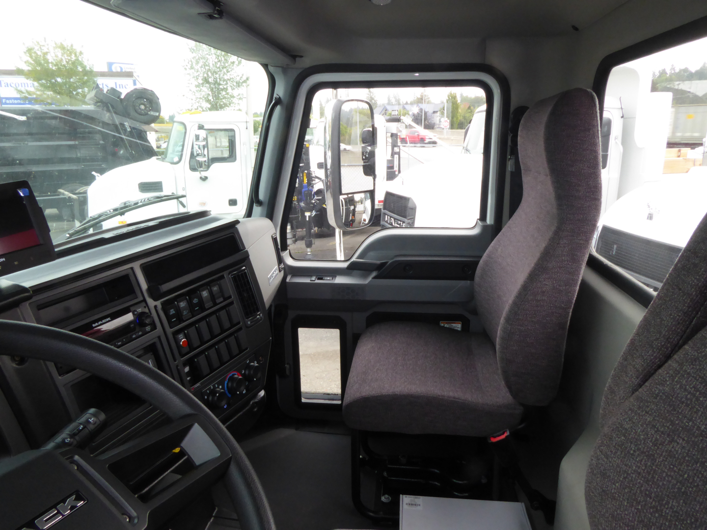 Truck cab interior of a 2025 Mack MD7 showing driver seat, steering wheel, and dashboard in view.
