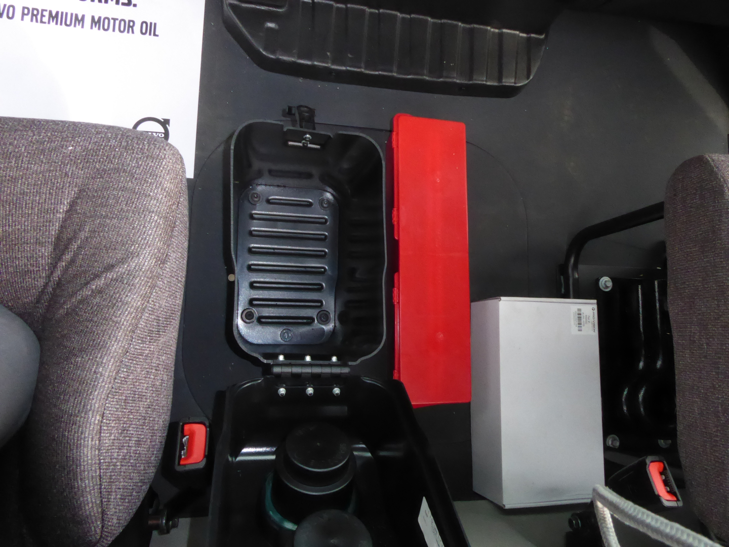 Mack MD7 cab interior showing control panel and vertical console with red safety latch and a silver rectangular component; partial view of seats and floor mat.