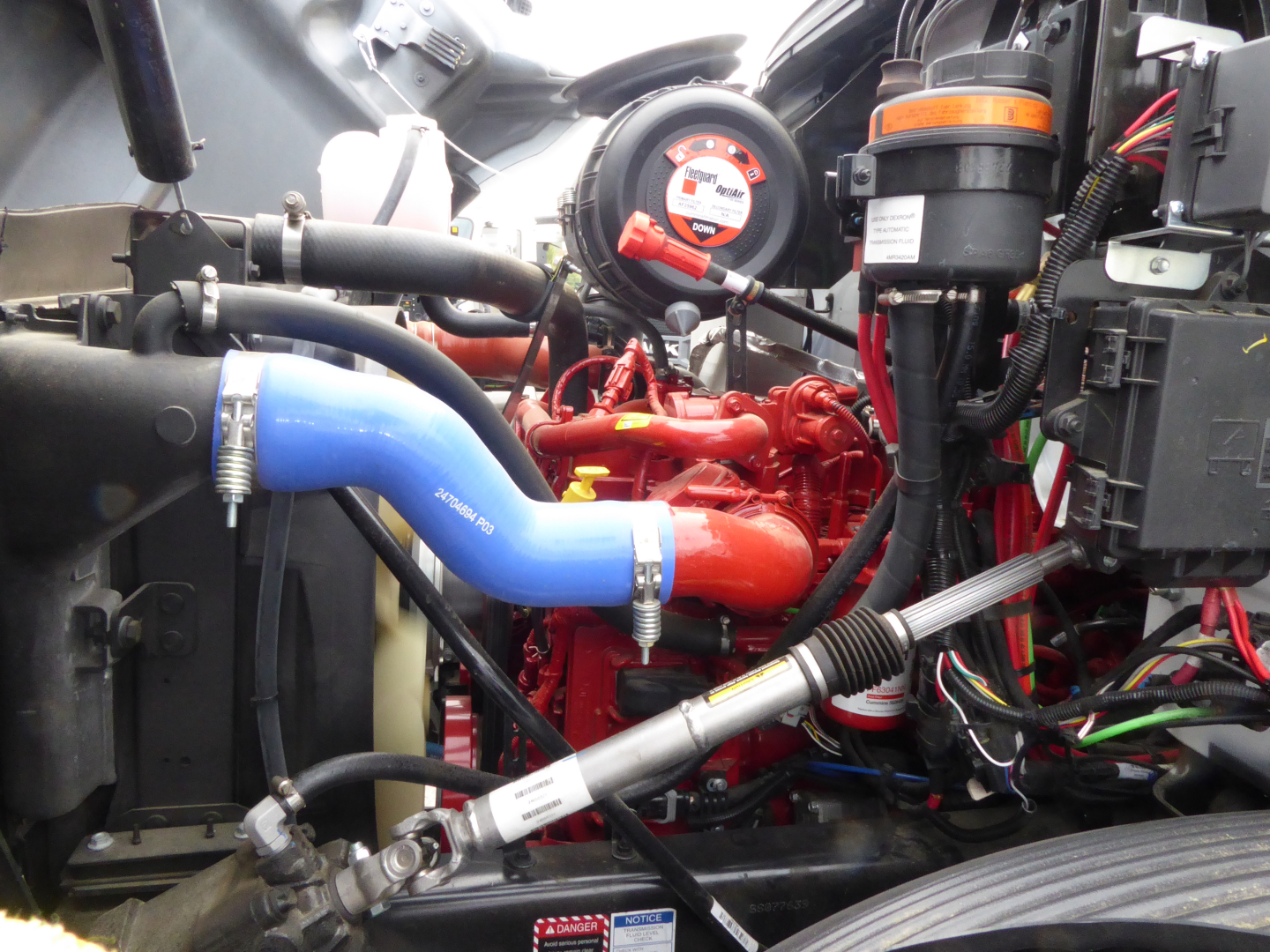 Mack MD7 engine bay with red engine, blue coolant hose, black hoses, and electrical harnesses visible.