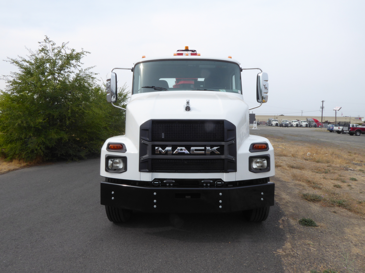 Front view of white 2025 Mack MD7 truck with large grille, headlights, and Mack emblem; front bumper and large mirrors visible.