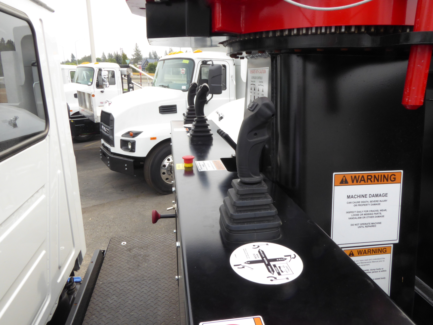 Truck cab and a grapple crane on a heavy equipment truck showing a control lever, amber warning labels, and circular props on a black surface.