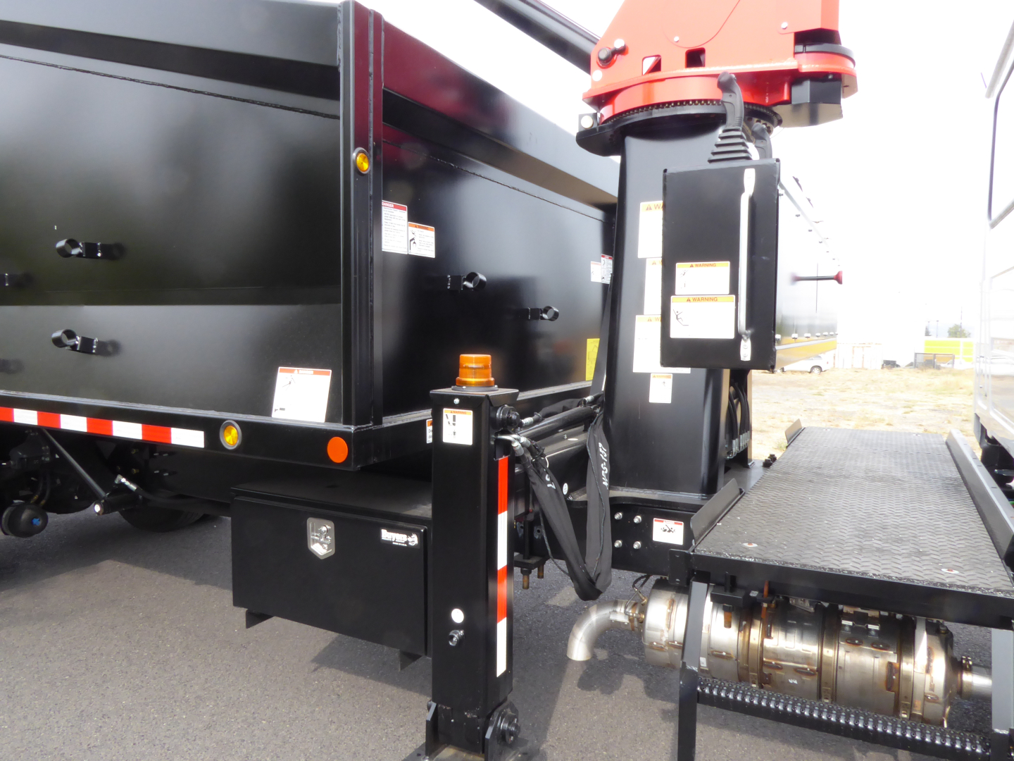 Mack MD7 truck with grapple equipment showing hydraulic system, black toolbox, and red grapple actuator on a flatbed truck.