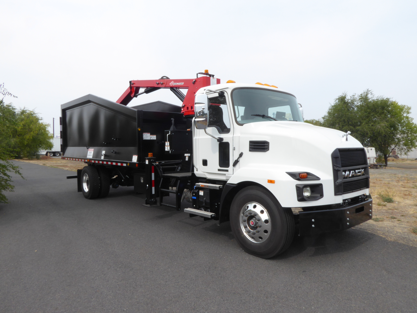 Mack MD7 truck with a grapple attachment viewed from the side, white cab, black dump bed, red hydraulic arm.