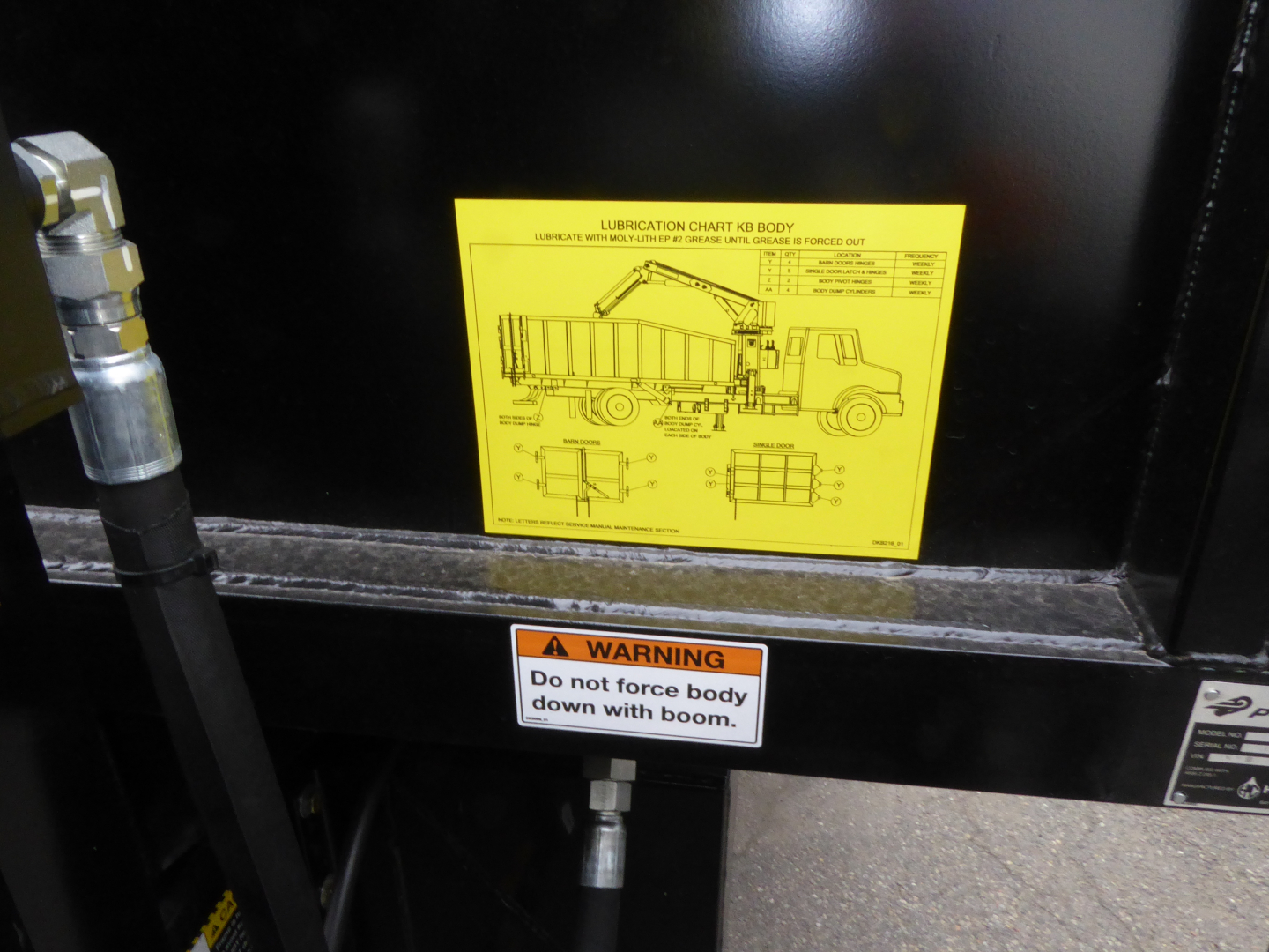 Grapple truck body showing a yellow lubrication chart label and warning sticker on the side of a Mack MD7 truck component.