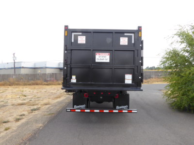 Back view of a black dump truck bed on a Mack MD7 chassis with warning labels and rear lights.