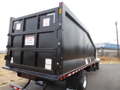 New 2025 Mack MD7 grapple truck rear and side view showing solid black dump bed and rear safety stickers.