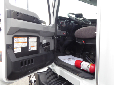 Truck cab interior from driver side showing open door, dashboard, steering wheel, and a fire extinguisher on the floorboard.