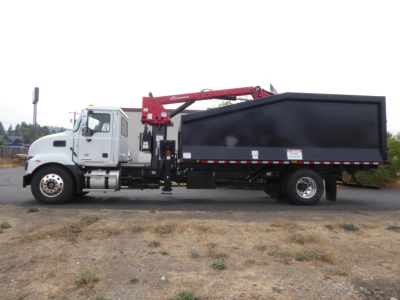 Truck side view showing a white cab and a large black dump body with a red crane, Mack MD7 class tag, and hydraulic lines.