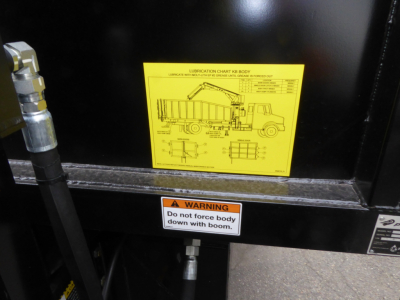 Grapple truck body showing a yellow lubrication chart label and warning sticker on the side of a Mack MD7 truck component.