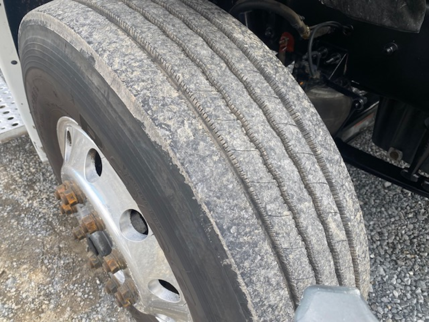 Truck wheel and front suspension area showing a worn dirt-coated dual-tire tread with dual rear axles and lug nuts visible.