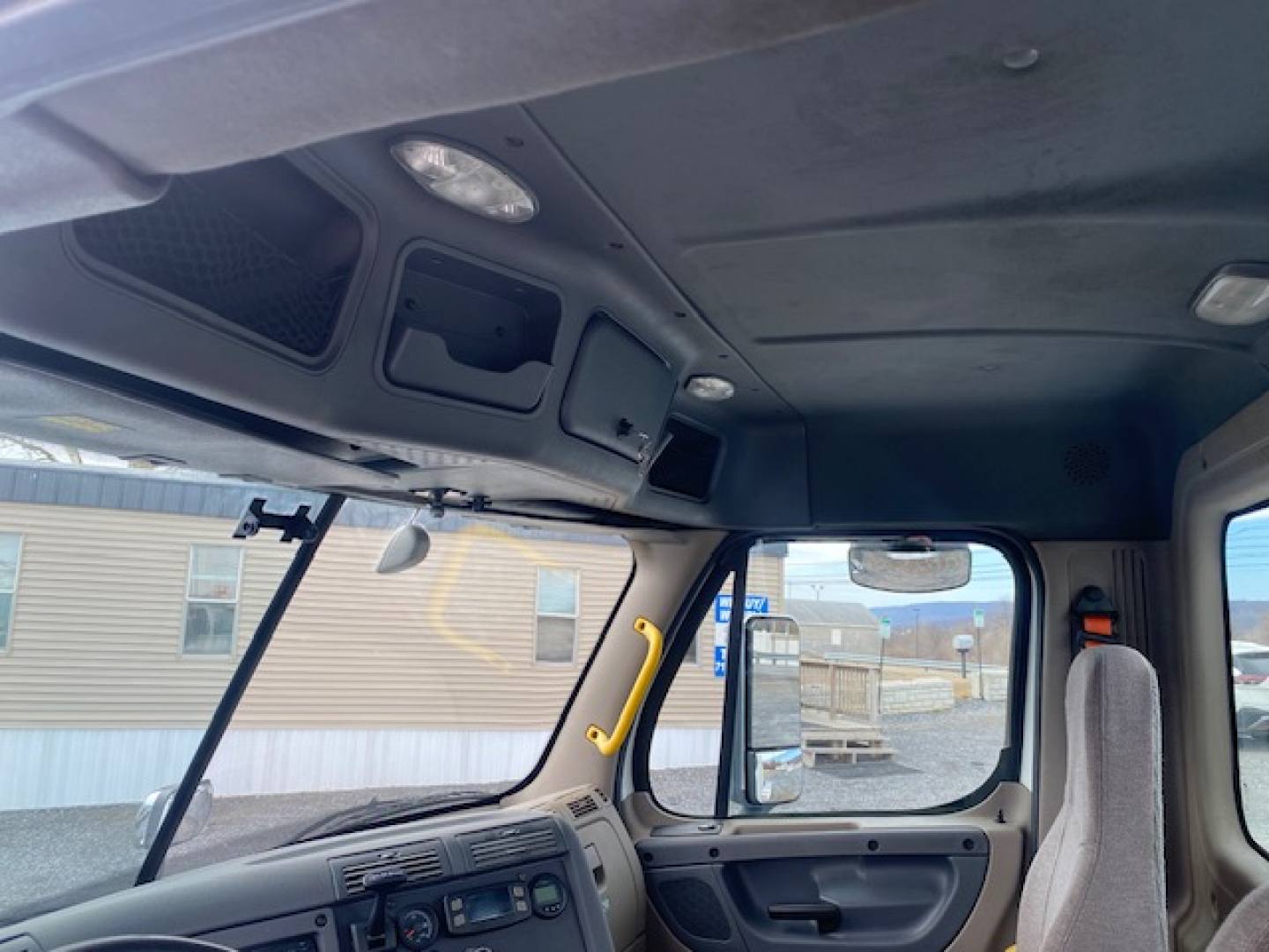 Cab interior of a 2016 Freightliner Cascadia 113 daycab, overhead console with storage compartments, sun visor area, dashboard with vents and controls visible.