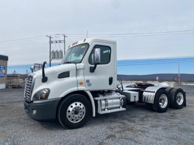 2016 Freightliner Cascadia 113 cab with dual rear axles, front view showing Freightliner badge, cab steps, and fuel tanks; vehicle on gravel lot.