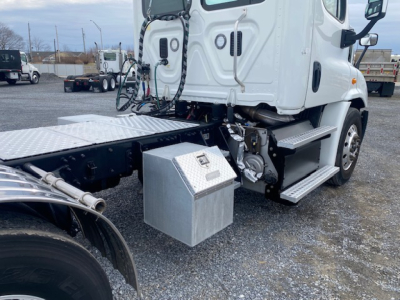Truck cab and side platform of a white 2016 Freightliner Cascadia 113 with a metal toolbox mounted beside the frame and exposed engine components.